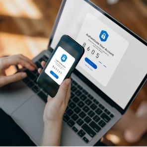 A phone verification number is held next to a laptop to authenticate a secure payment