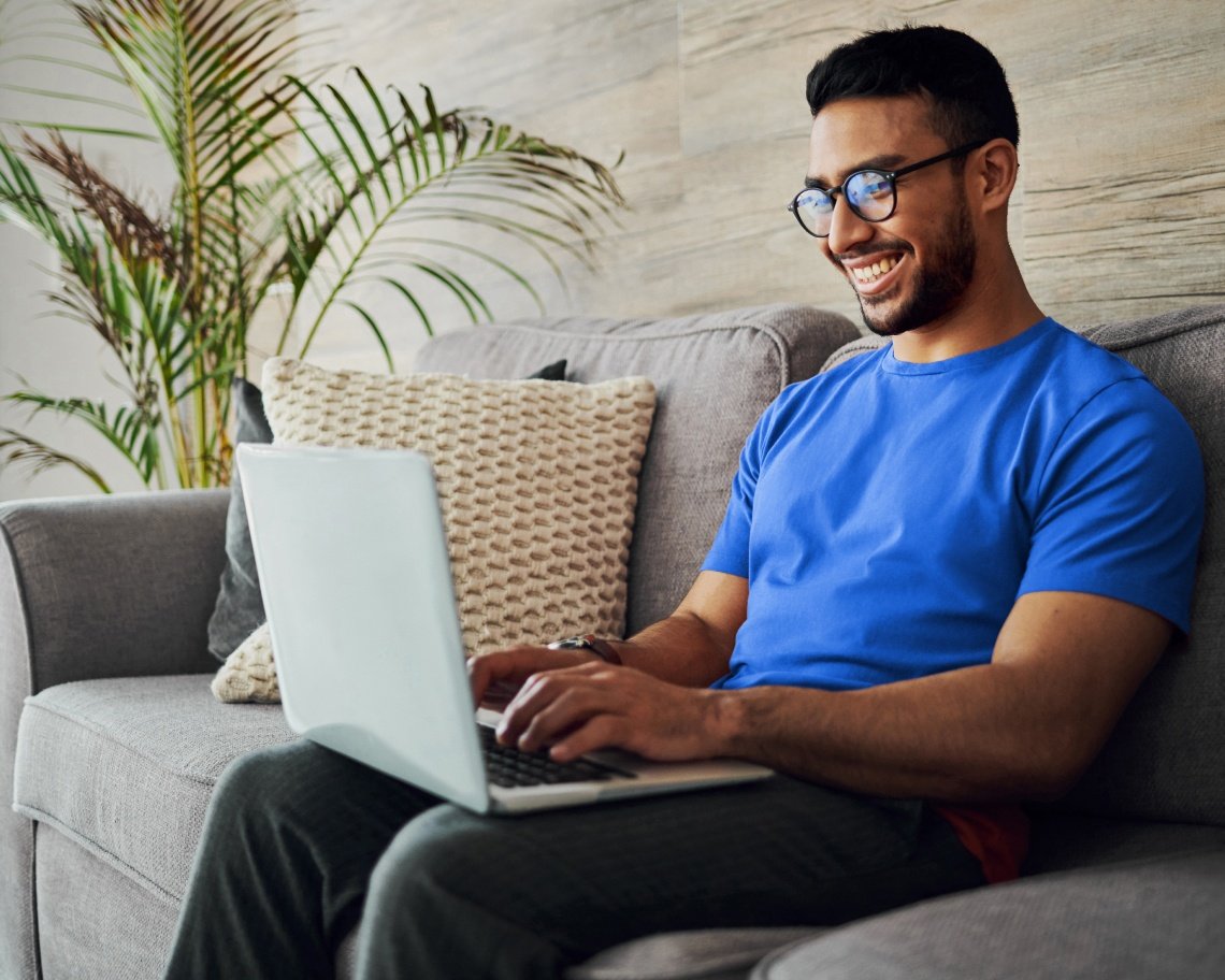 Smiling customer typing on a laptop on his couch