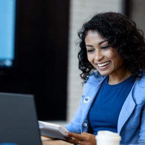 A smiling woman examines paperwork at a laptop