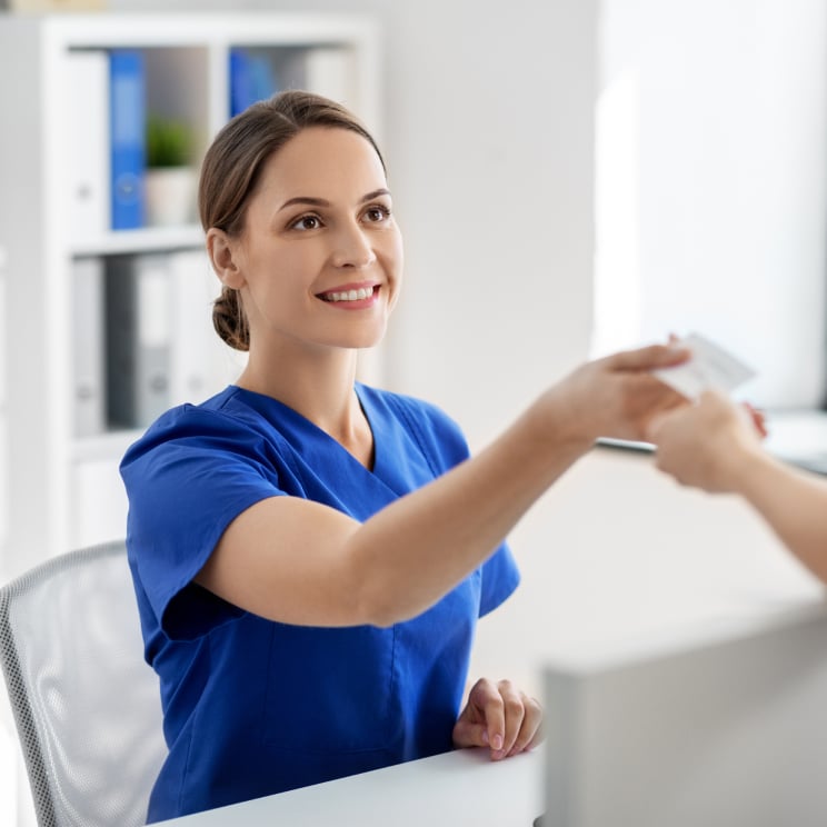 Healthcare employee at front desk taking card from patient