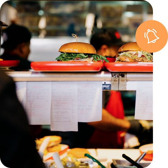 Food counter showing a line of tickets and two sandwiches on trays ready for pickup