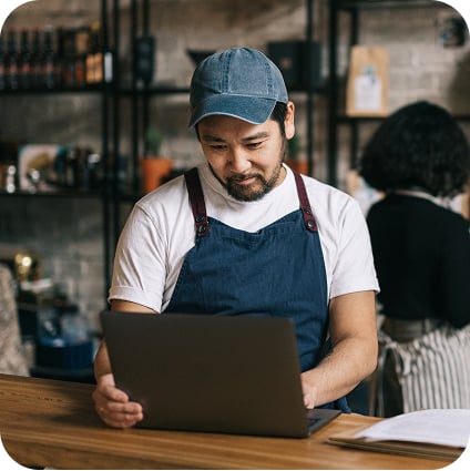 A person wearing an apron looks at an open laptop screen and smiles.