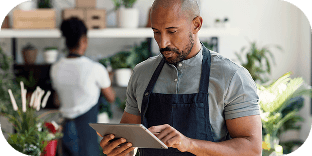 A person using a tablet while their coworker organizes plants on a shelf.