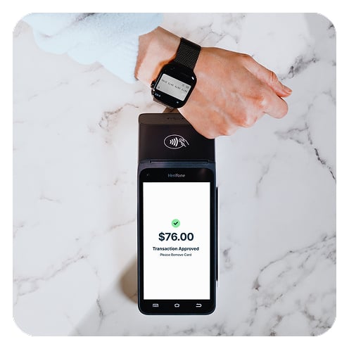 Closeup of a person tapping their smartwatch digital wallet on a black mobile payment terminal to pay