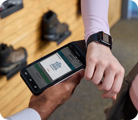 Closeup of a person wearing a smartwatch taping a handheld payment terminal to pay