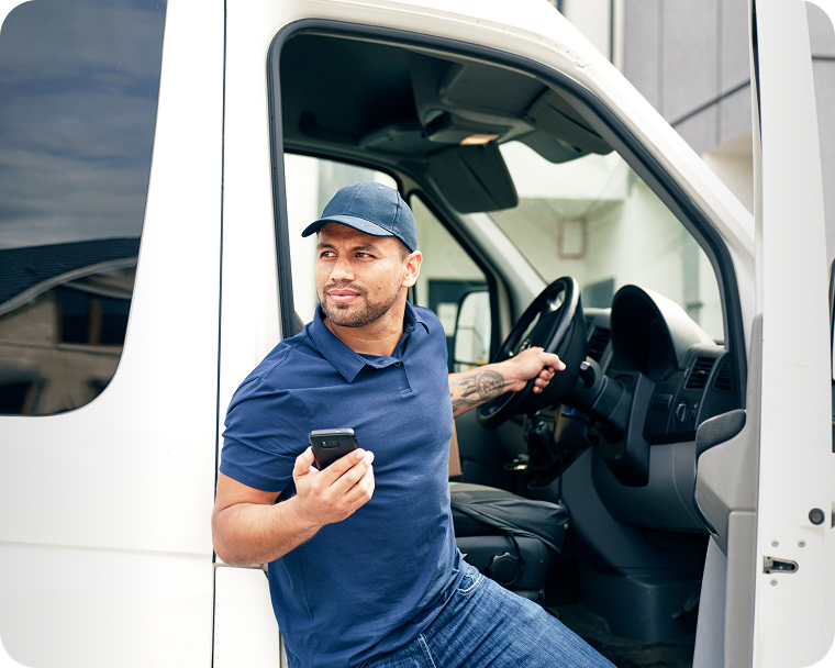 A person making deliveries holds a smartphone and exits the delivery vehicle. 