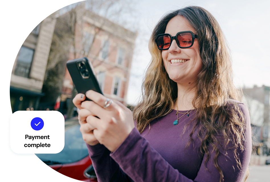 A woman smiles down at the phone in her hand as a graphic with a checkmark and the words payment complete overlay the scene.