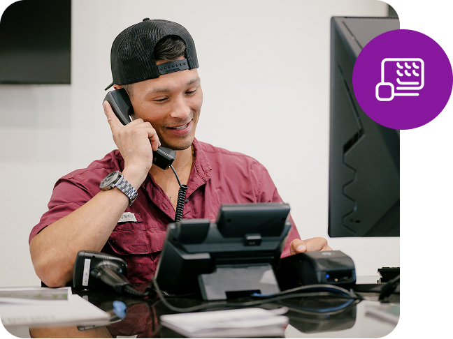 A man sits at a counter and smiles as he holds an office phone to his ear and a small circle graphic icon overlays the image.
