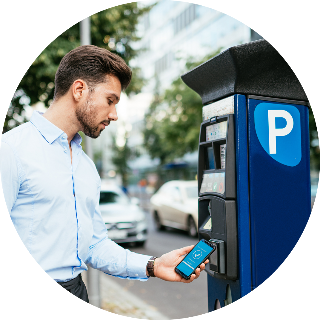 A man holds his mobile device up to a parking payment kiosk to make a NFC transaction and reserve his parking spot.