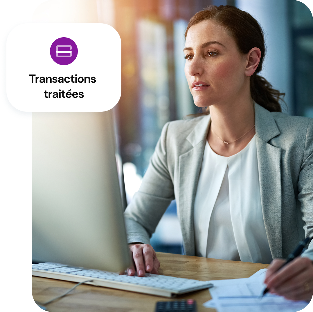 Une femme est assise à une table devant un ordinateur de bureau, et un graphique superposé indique “transaction traitée”