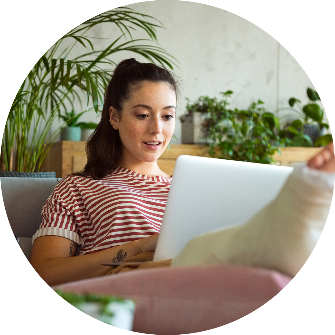 A woman with a cast on her foot sits with a laptop in her lap.