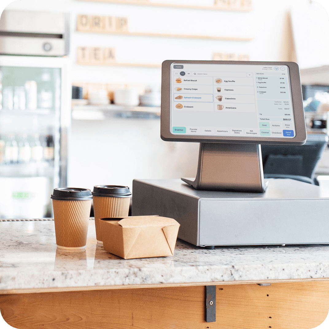 Retail POS machine on counter next to two coffees and a box
