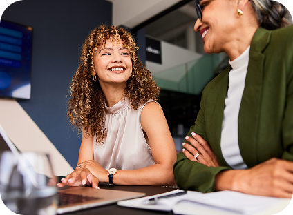 Two people smiling at each other while using a laptop in an office.