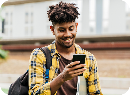 A student smiling while using their cell phone on a university campus.