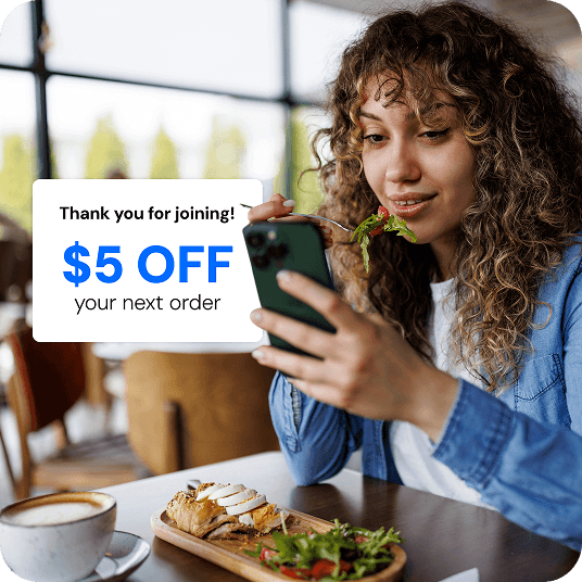 Restaurant customer signing up for a loyalty program on her phone while dining in. A popup screen reads “Thank you for joining! $5 OFF your next order”
