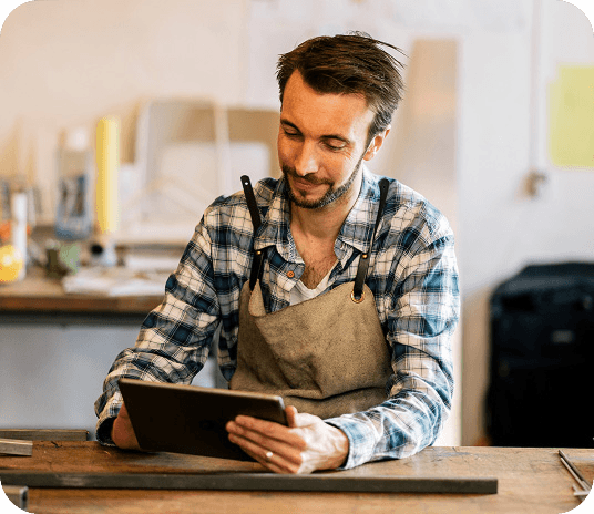 Small business employee wearing an apron, sitting at a table and looking down at a Genius tablet point of sale