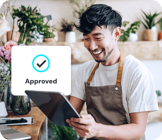 Plant store employee smiling while looking down at a mobile POS. A popup window shows an “Approved” transaction.