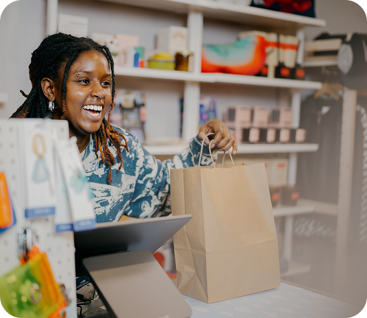 Worker hands customer their purchase in a bag after checking out at the countertop point of sale. 