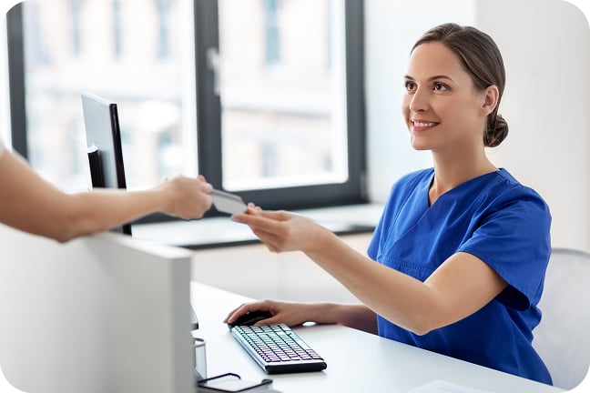 Woman in scrubs at front desk in medical office with patient handing her their card to pay