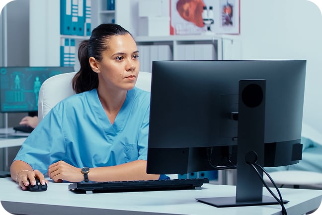 Woman wearing scrubs sitting at a desk using laptop in medical office