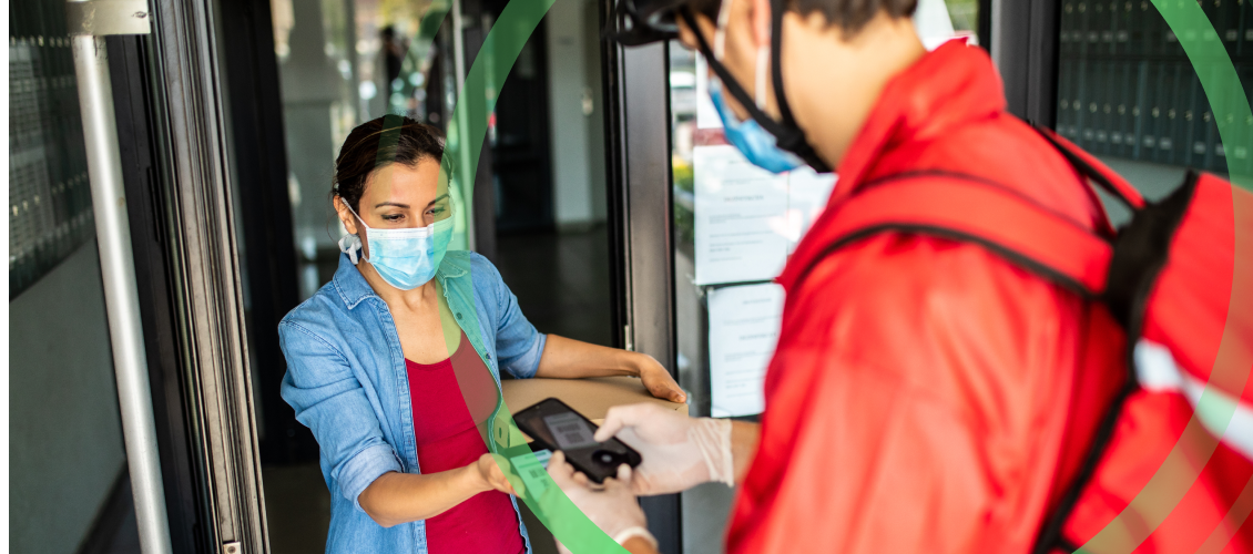 Customer wearing mask receiving food order from delivery worker wearing protective gear
