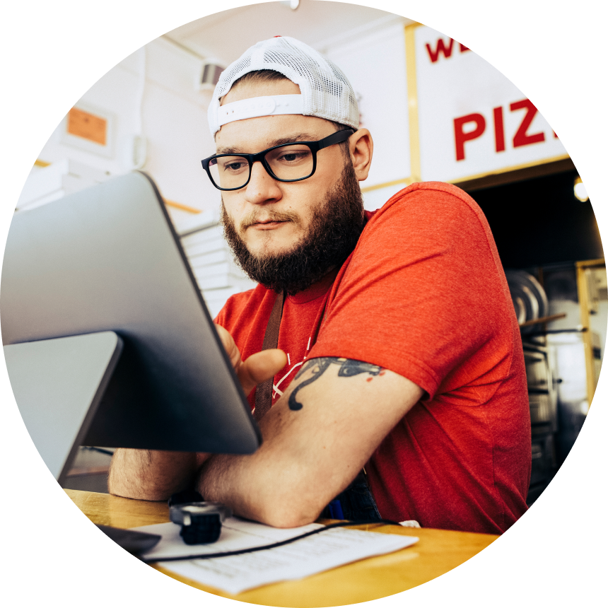 Pizzaville employee in glasses and red company-branded shirt working at countertop point of sale terminal