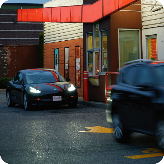 Cars line up in a fast food drive thru at night.