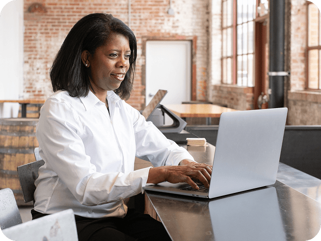 Woman sitting at counter in restaurant smiling and typing on a laptop computer