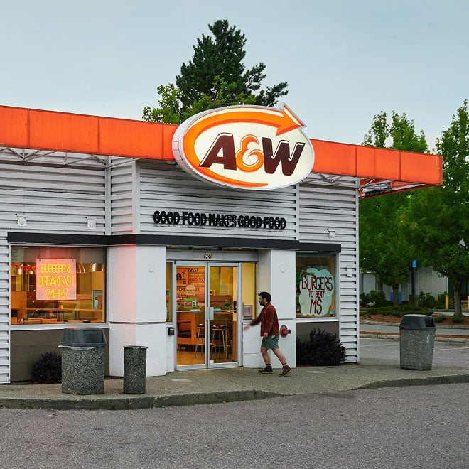 A customer enters the front door of an A&W restaurant while customers in their cars order via the drive thru.