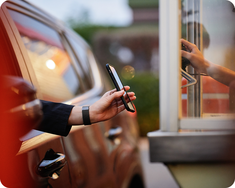 A quick service employee accepts a customer’s mobile payment in the drive thru.