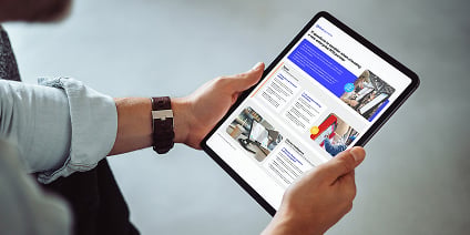 Hands holding a tablet showing a report spread with blue headings, body text, and multiple photos.