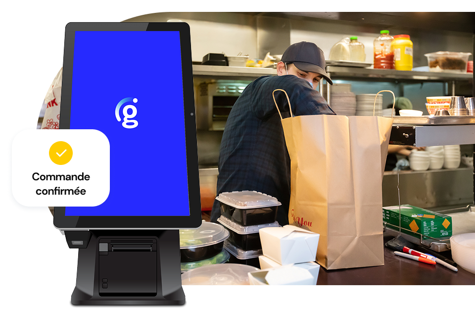 A look at a busy kitchen scene featuring a person stacking takeaway containers in a large brown bag; a Genius kiosk with a small UI call-out that says “Order confirmed” sits in the foreground.