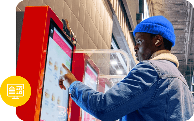A person wearing a blue beanie and denim jacket selects a food item from a red kiosk.