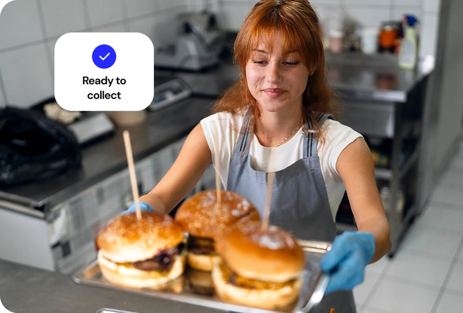 Restaurant kitchen worker serves up plate of burgers to server.