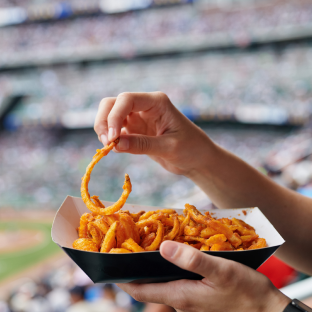 An image of a basket of curly fries in the foreground, with a packed stadium in the background.