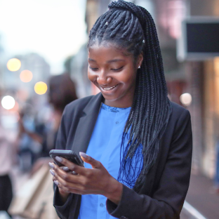 A smiling businesswoman looks down at her smart phone.