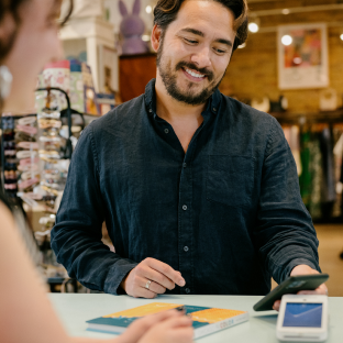 A smiling person completes a payment with their smart phone on a handheld POS device.