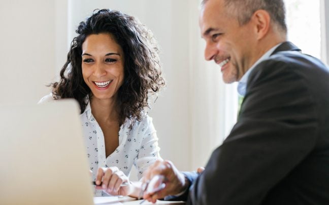 A man and a woman smiling while looking at a laptop