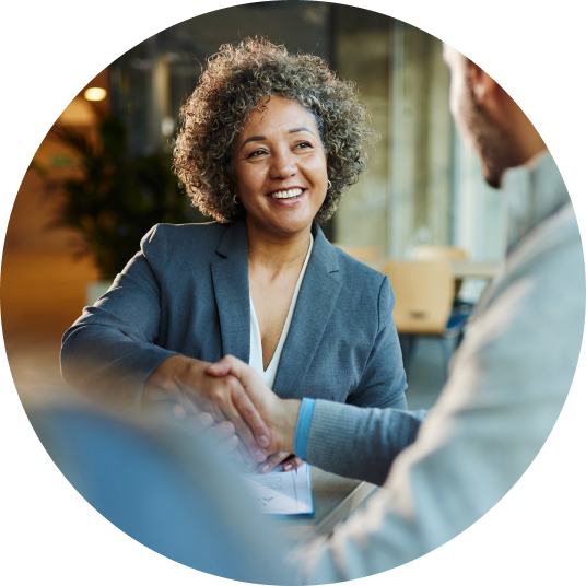 A smiling woman in a blazer shakes a man’s hand.