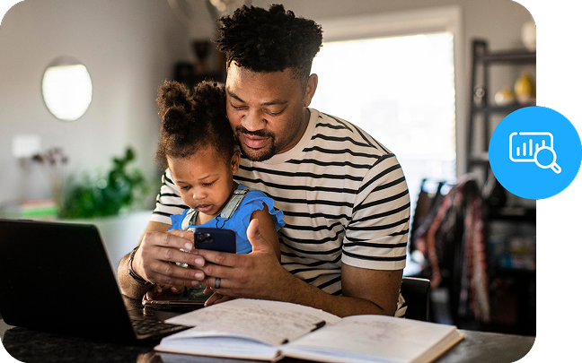 A parent holds a baby over a desktop, while studying.