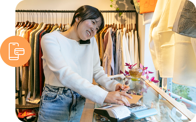 A clothing retailer takes a payment while talking on a mobile phone.