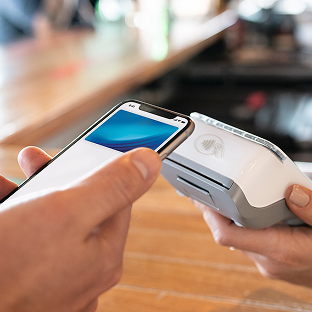 A customer swipes a phone over a card machine to make a payment.