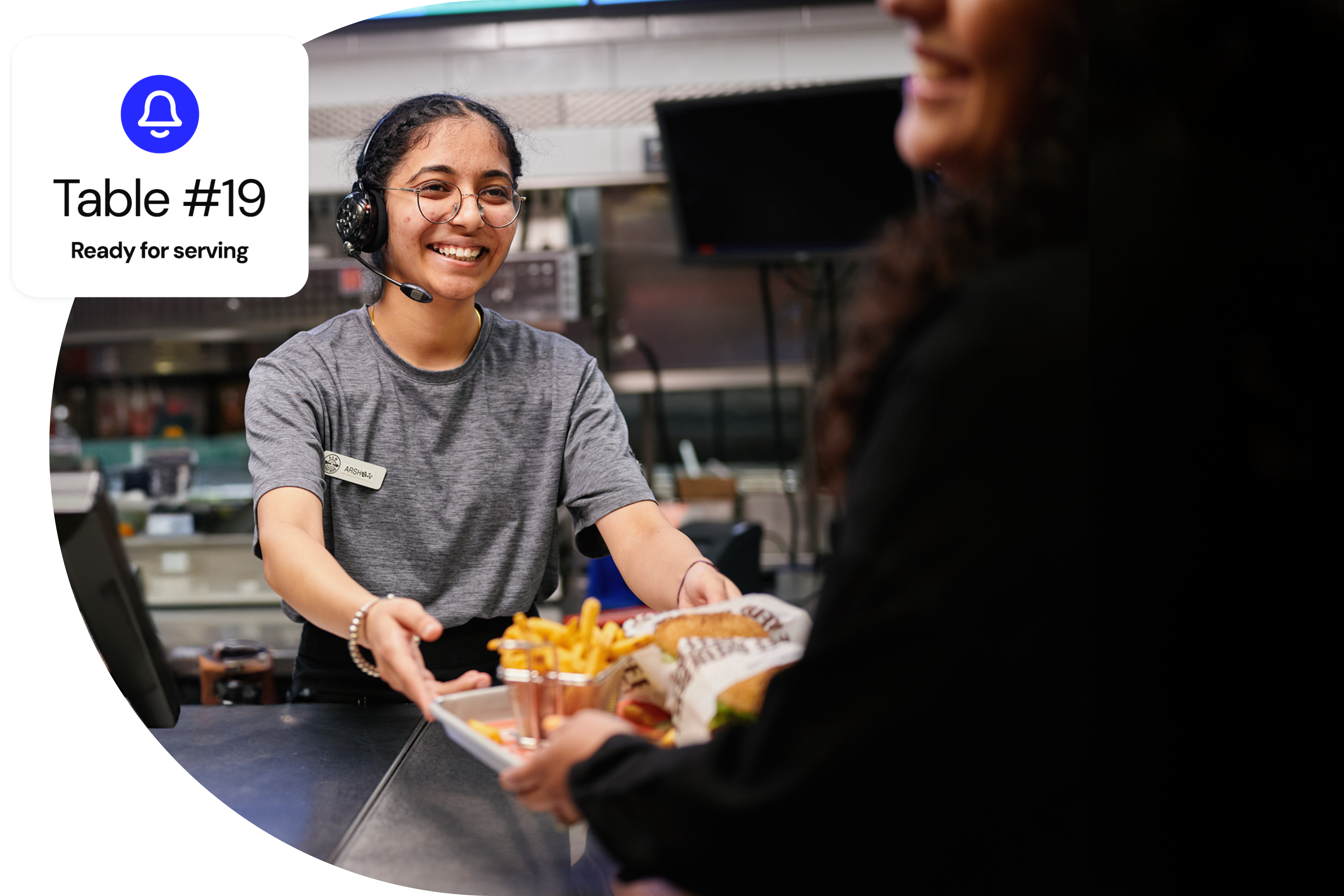 A quick service restaurant employee smiling while handing out an order to a customer.