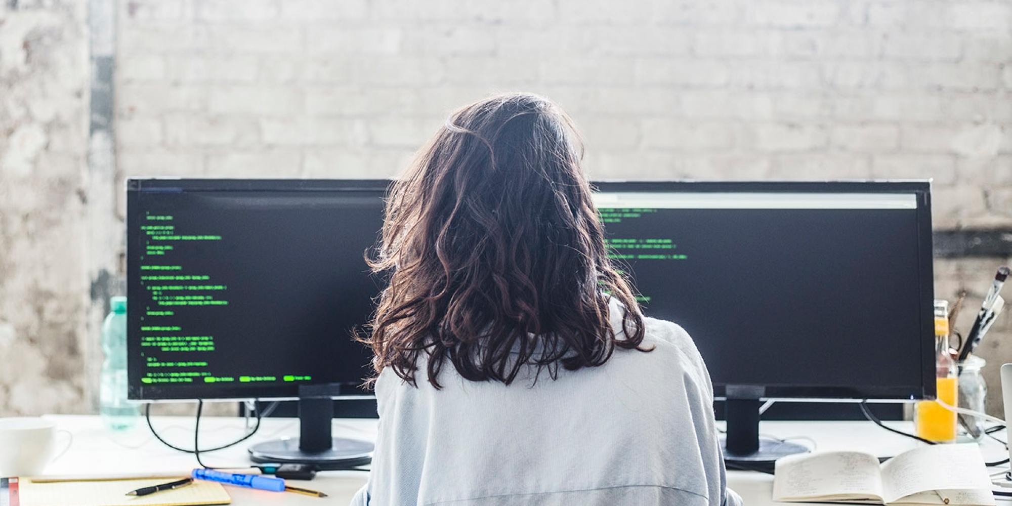 Image of person working at desk with two computer monitors displaying lines of code