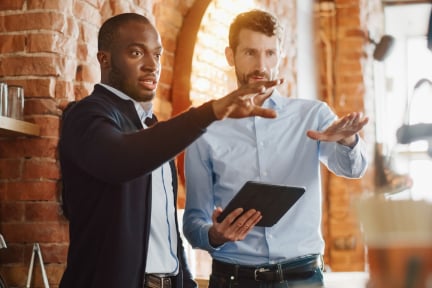 Two men in an office environment talking and looking at a tablet