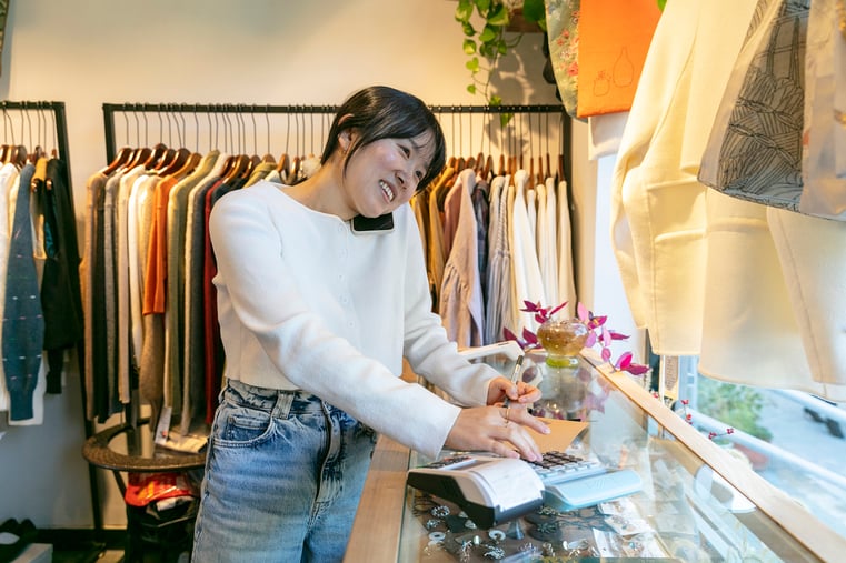 Smiling person working behind counter of clothing boutique while talking on phone