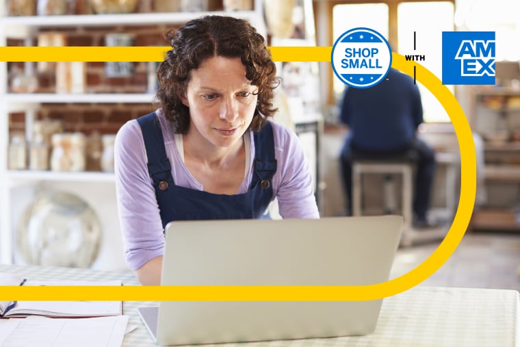 Retail worker in casual clothes working intently on laptop inside brightly lit small business