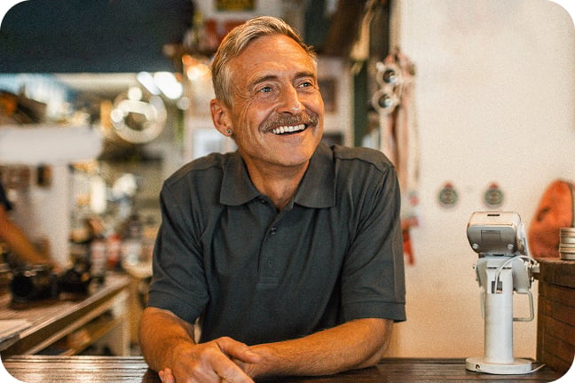 Smiling small-business owner leans on wooden counter next to point of sale device