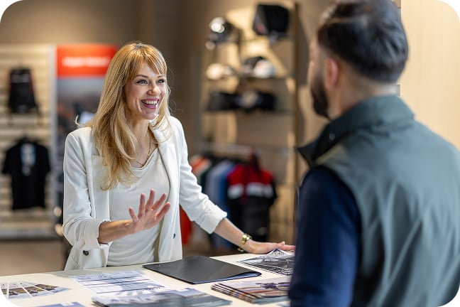 Retail worker assists customer with brochures and paperwork across counter in retail showroom