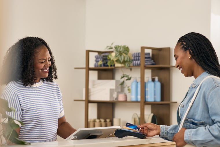 Merchant stands behind counter in retail setting as customer holds card to device ready to use tap to pay